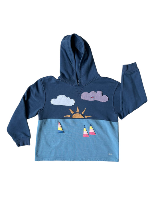 A sweatshirt with a graphic design of ocean waves, clouds, sun and a whale tail